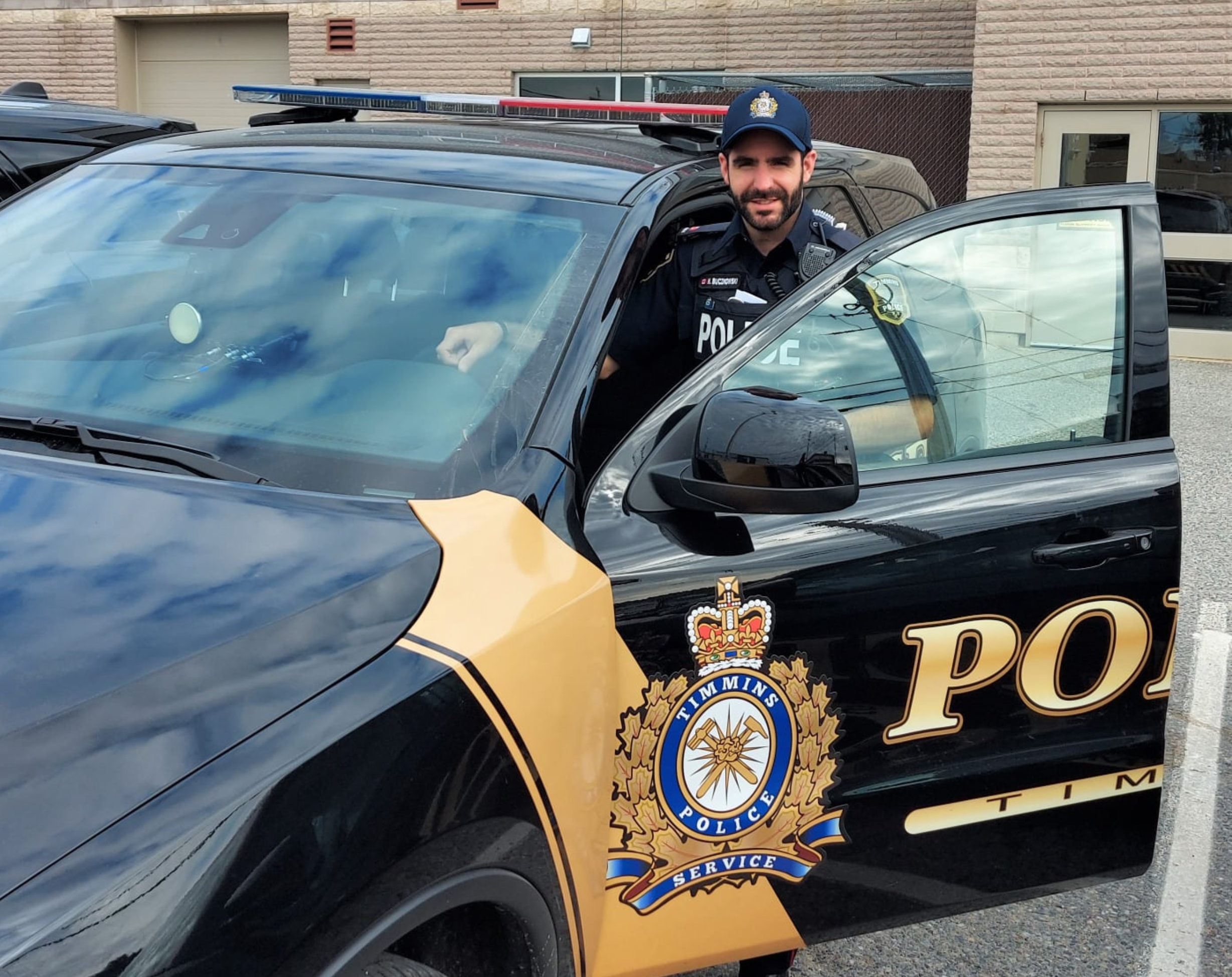 A Timmins Police officer standing in front of a police car.